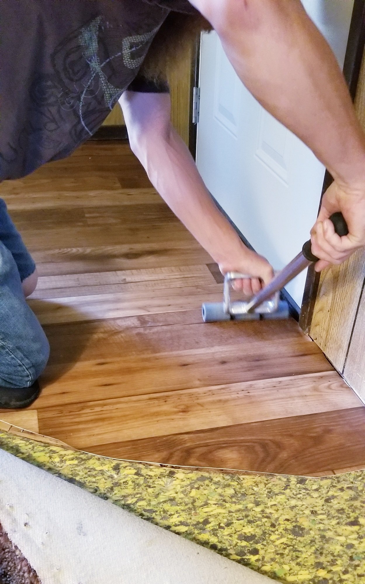A person using a tool to install hardwood flooring near a doorframe.