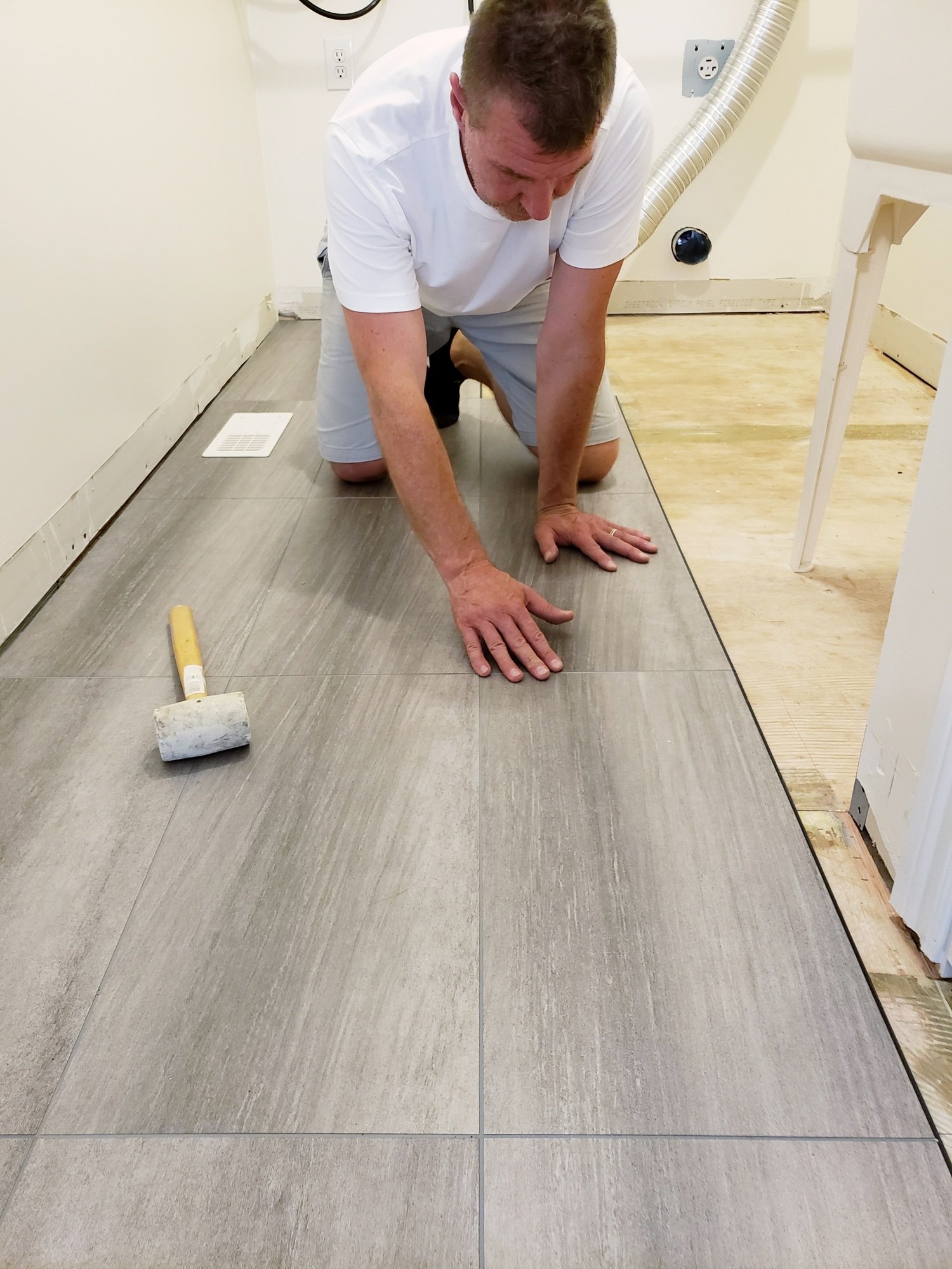 Man kneeling on gray tiles, applying pressure with his hands, a mallet beside him.