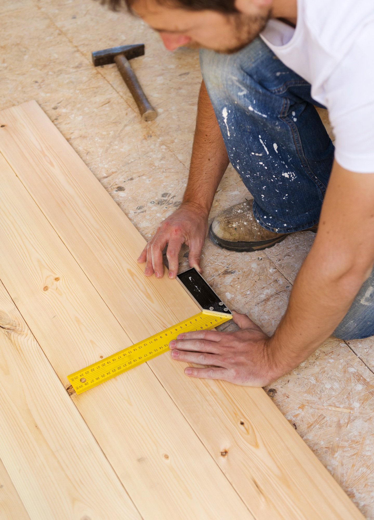 Man using a square tool and measuring tape on wooden planks in a workshop.
