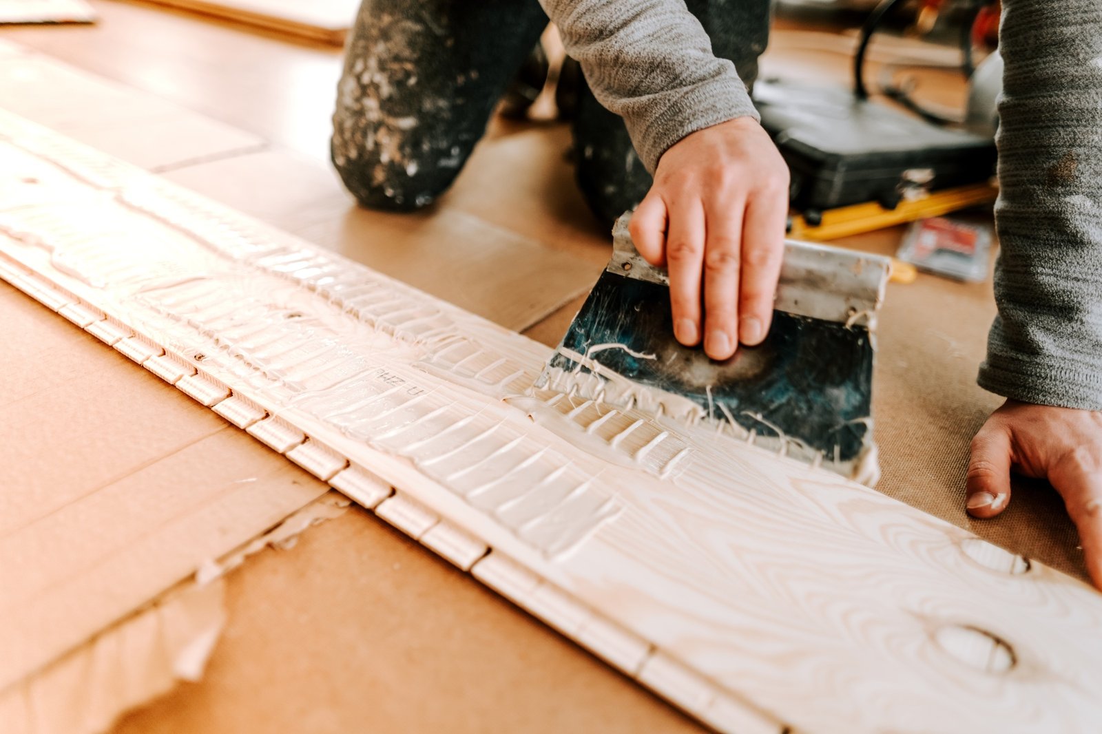 A person applying adhesive with a trowel on a wooden surface in a workshop setting.