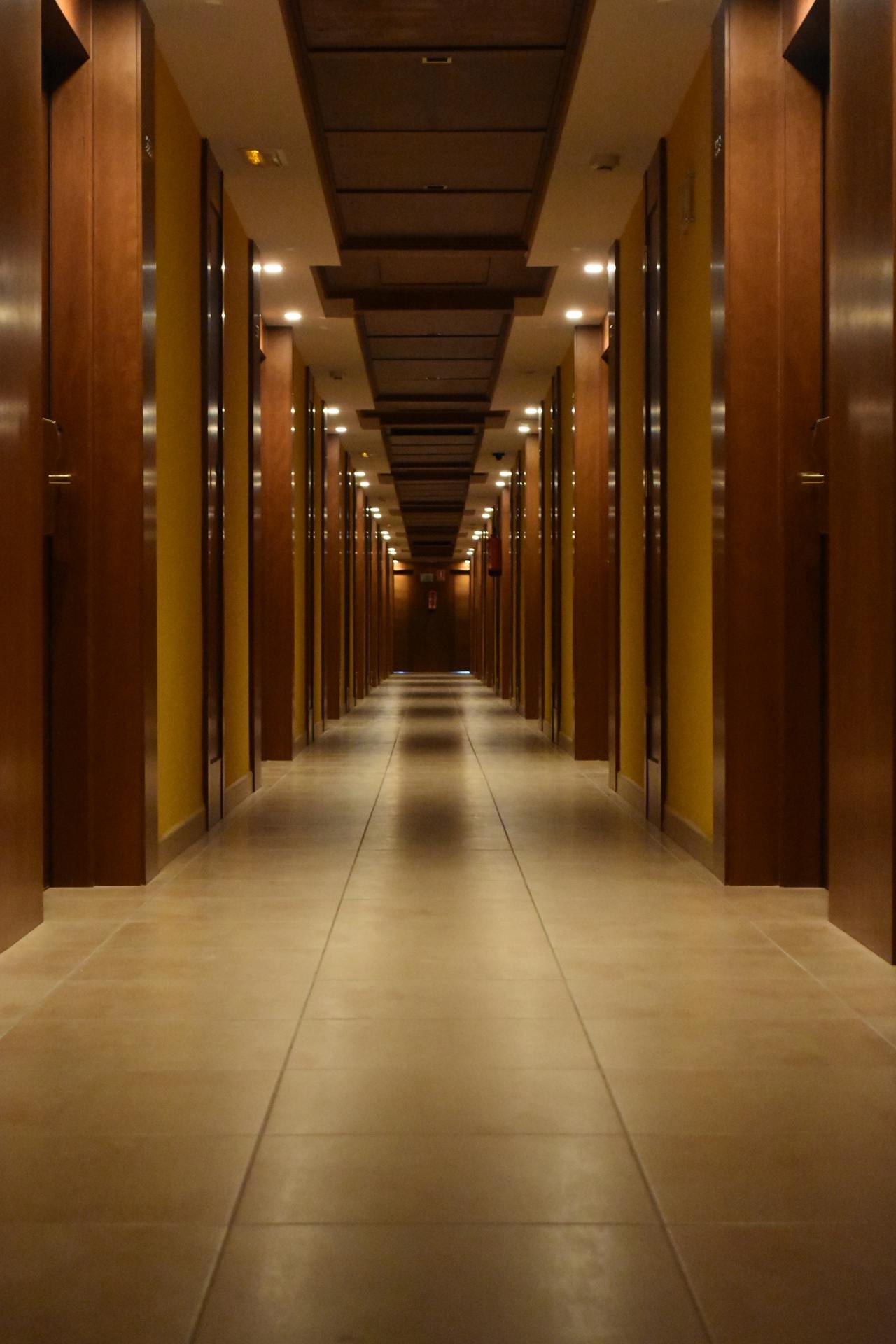 Long, well-lit hallway with wooden doors and neutral tile flooring.